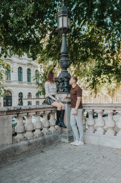 Budapest couple photoshoot: a green lamp and trees near the Basilica The couple beside a carved stone balustrade and green lamp beneath trees near St Stephen’s Basilica during a couple photoshoot in Budapest.