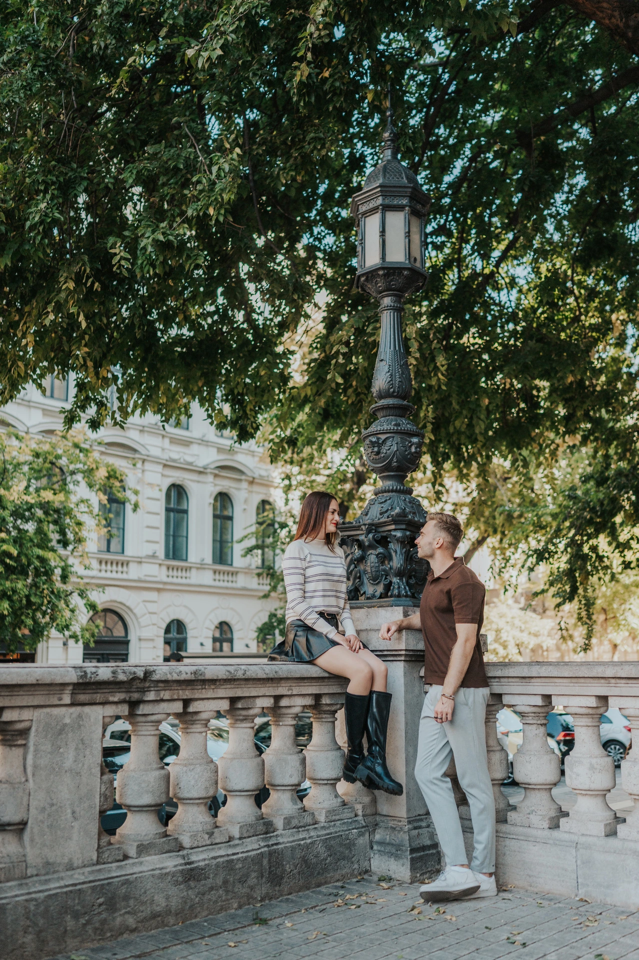 The couple standing close by a stone balustrade under trees near St Stephen’s Basilica during a couple photoshoot in Budapest.