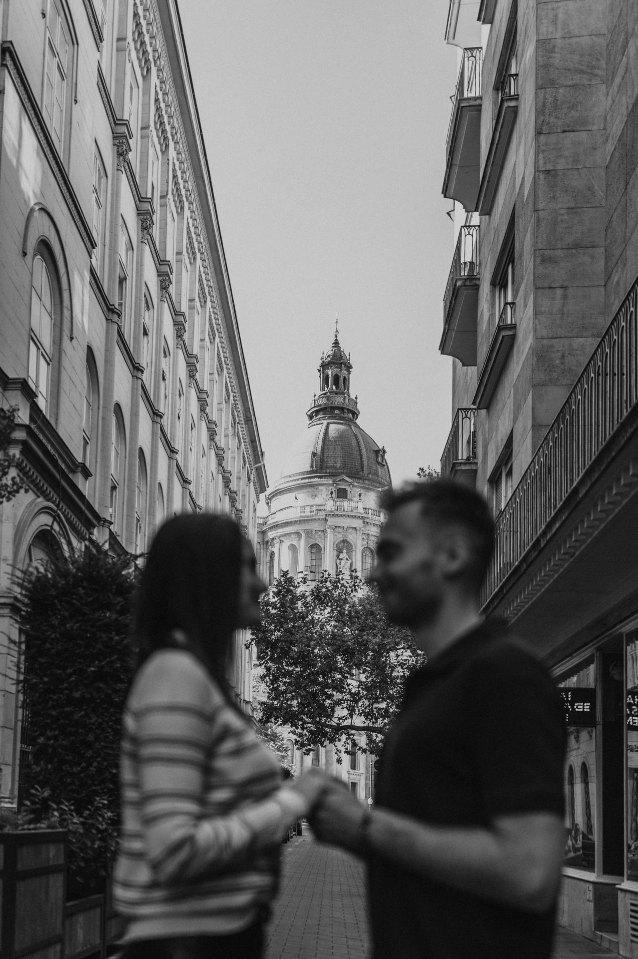 Soft-focus black-and-white portrait of the couple on a street with St Stephen’s Basilica beyond them during a couple photoshoot in Budapest.