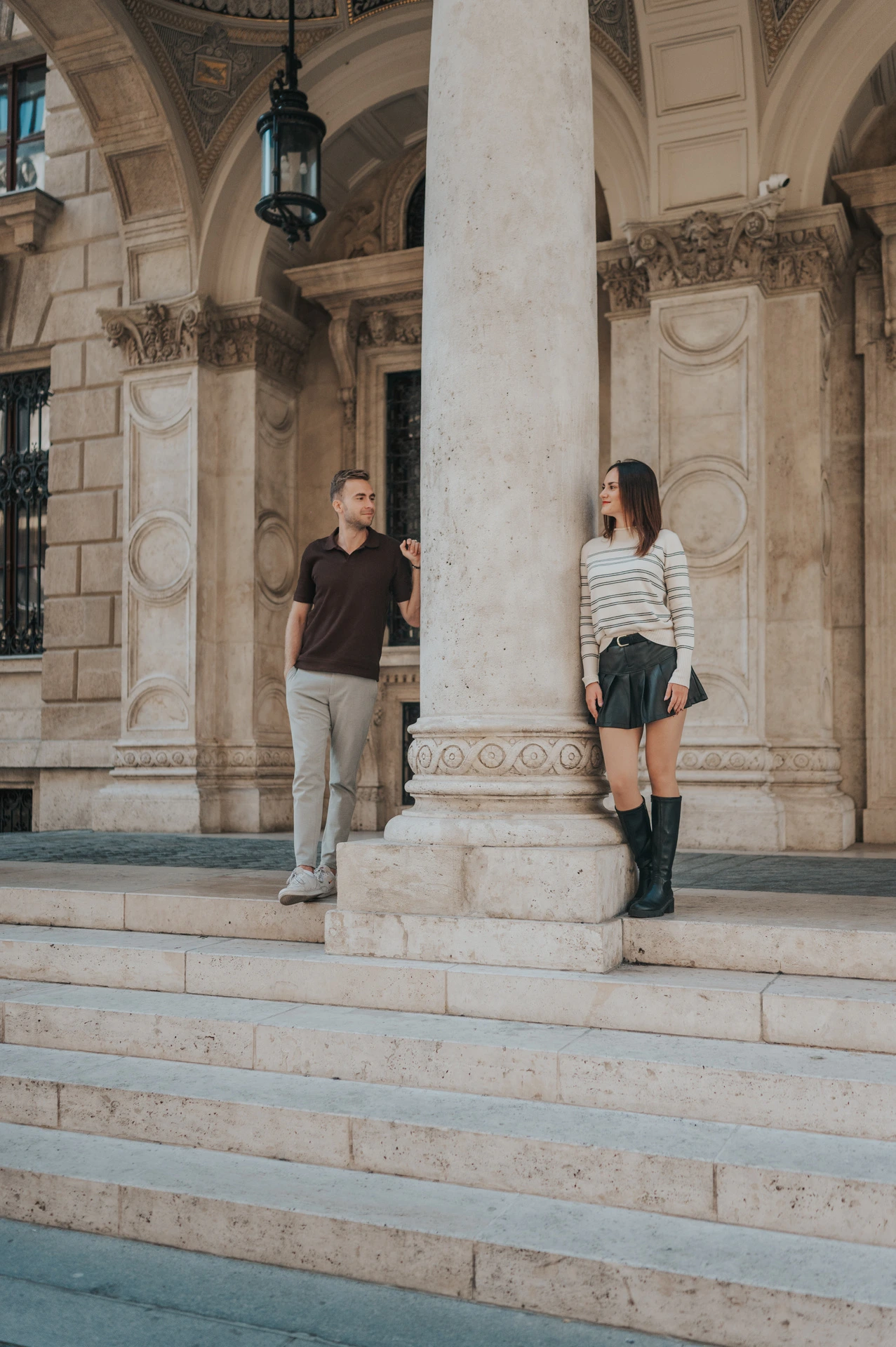 The couple leaning on opposite sides of a stone column outside the Opera during a couple photoshoot in Budapest.