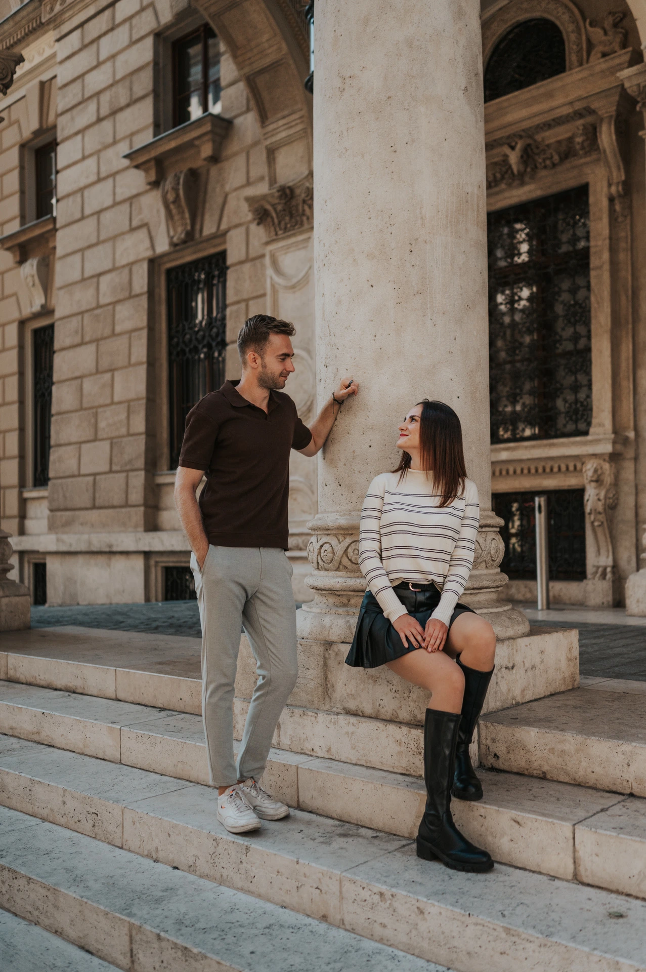 The couple looking towards each other beside a stone column on the Opera steps during a couple photoshoot in Budapest.