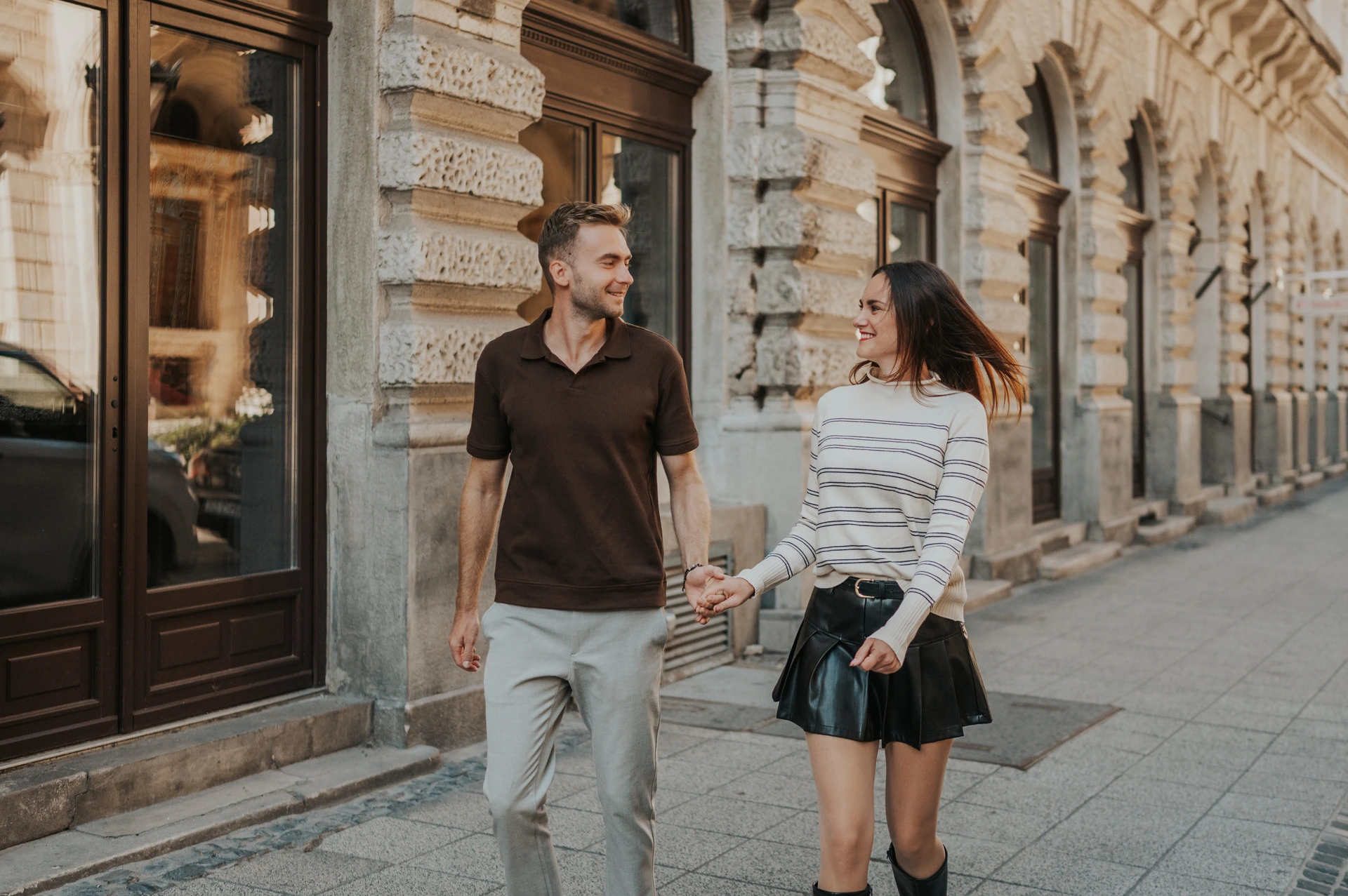 Budapest couple photoshoot: a wide portrait beside the Opera windows A landscape portrait of the couple walking hand in hand beside the Opera’s ornate windows during a couple photoshoot in Budapest.