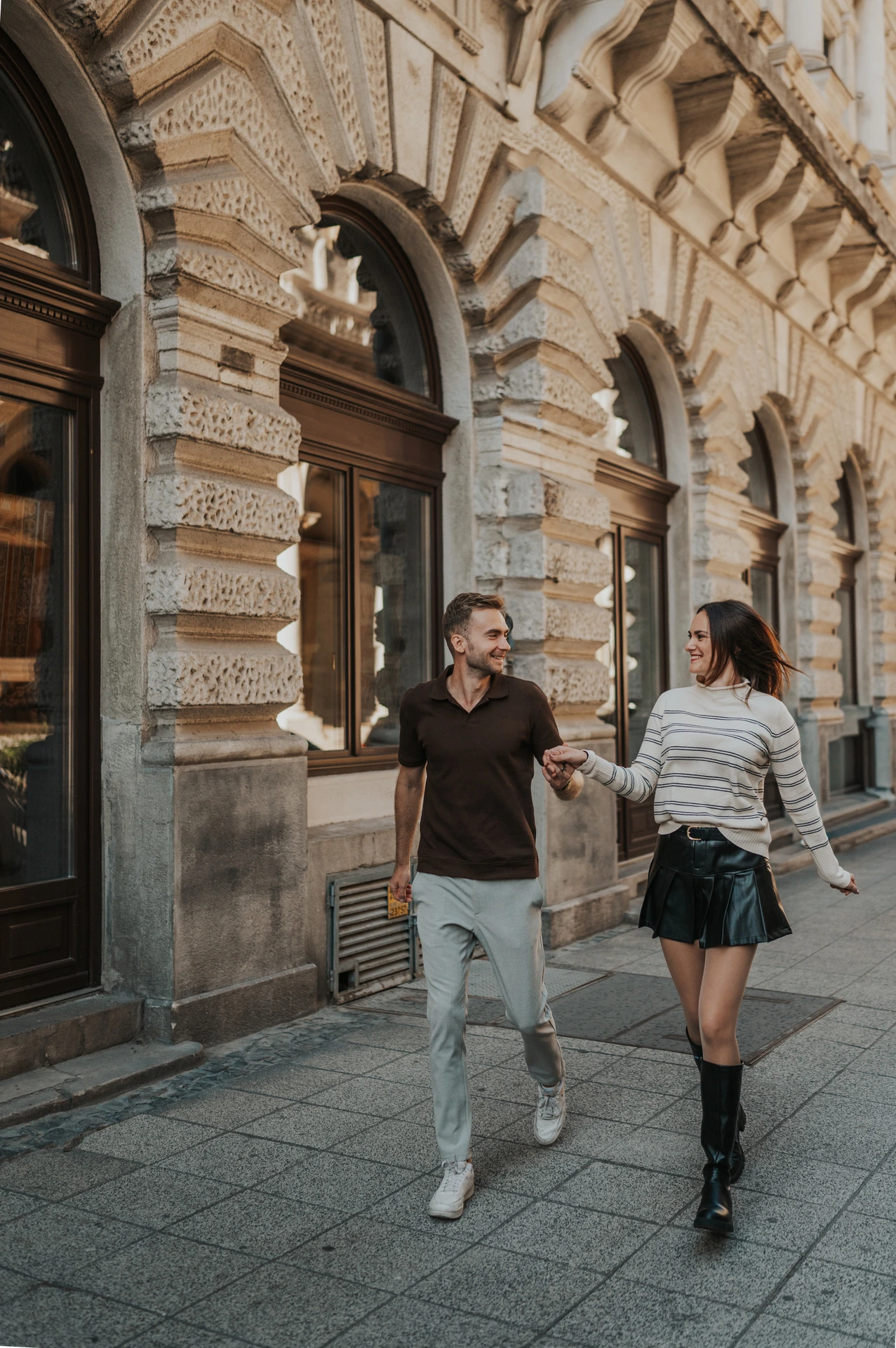 The couple walking beside the Opera’s ornate arched windows and carved stone façade during a couple photoshoot in Budapest.
