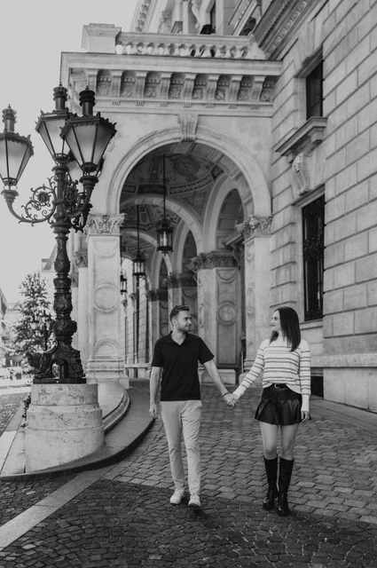 Budapest couple photoshoot: walking past the Opera arches in black and white Black-and-white photograph of the couple walking hand in hand past the Opera’s arched entrance during a couple photoshoot in Budapest.