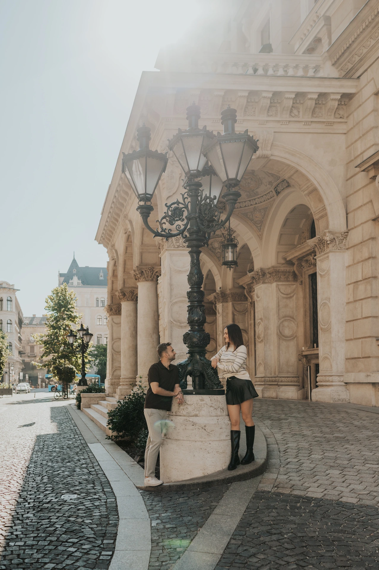The couple beside an ornate green street lamp and the Opera’s arched entrance during a couple photoshoot in Budapest.