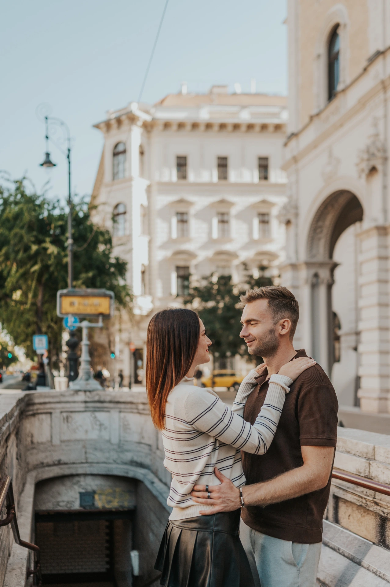 The couple embracing at the top of the stone steps to Opera metro station during a couple photoshoot in Budapest.