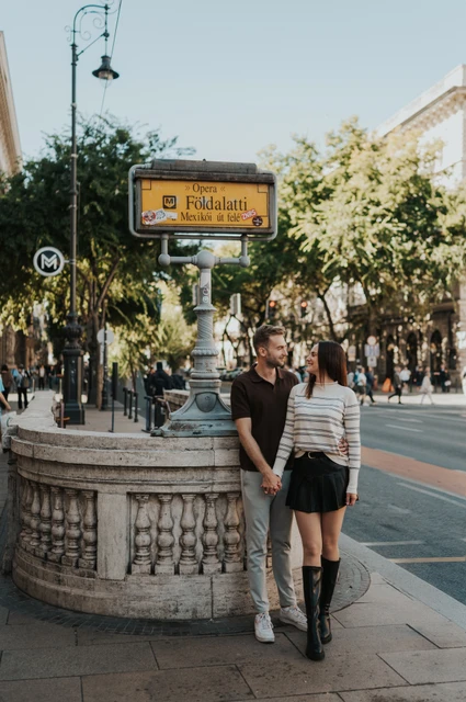 Budapest couple photoshoot: a close portrait at the Opera metro entrance A closer portrait of the couple beside the yellow Földalatti sign and stone metro balustrade during a couple photoshoot in Budapest.