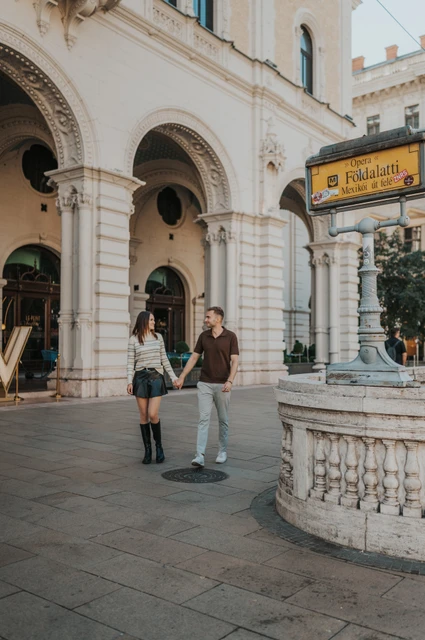 Budapest couple photoshoot: walking beside the Opera metro entrance The couple holding hands beside the Opera metro entrance and its yellow Földalatti sign during a couple photoshoot in Budapest.