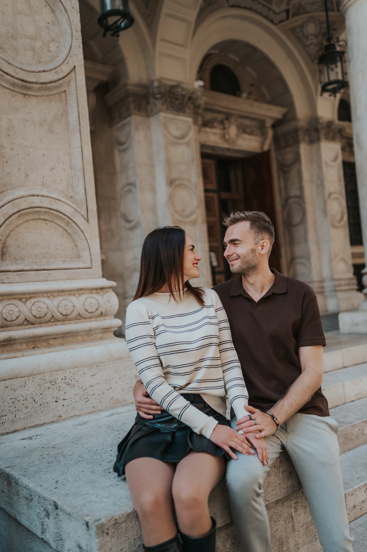 Budapest couple photoshoot: smiles beside the Opera’s carved stonework A close portrait of the smiling couple sitting on a stone plinth outside the Opera during a couple photoshoot in Budapest.