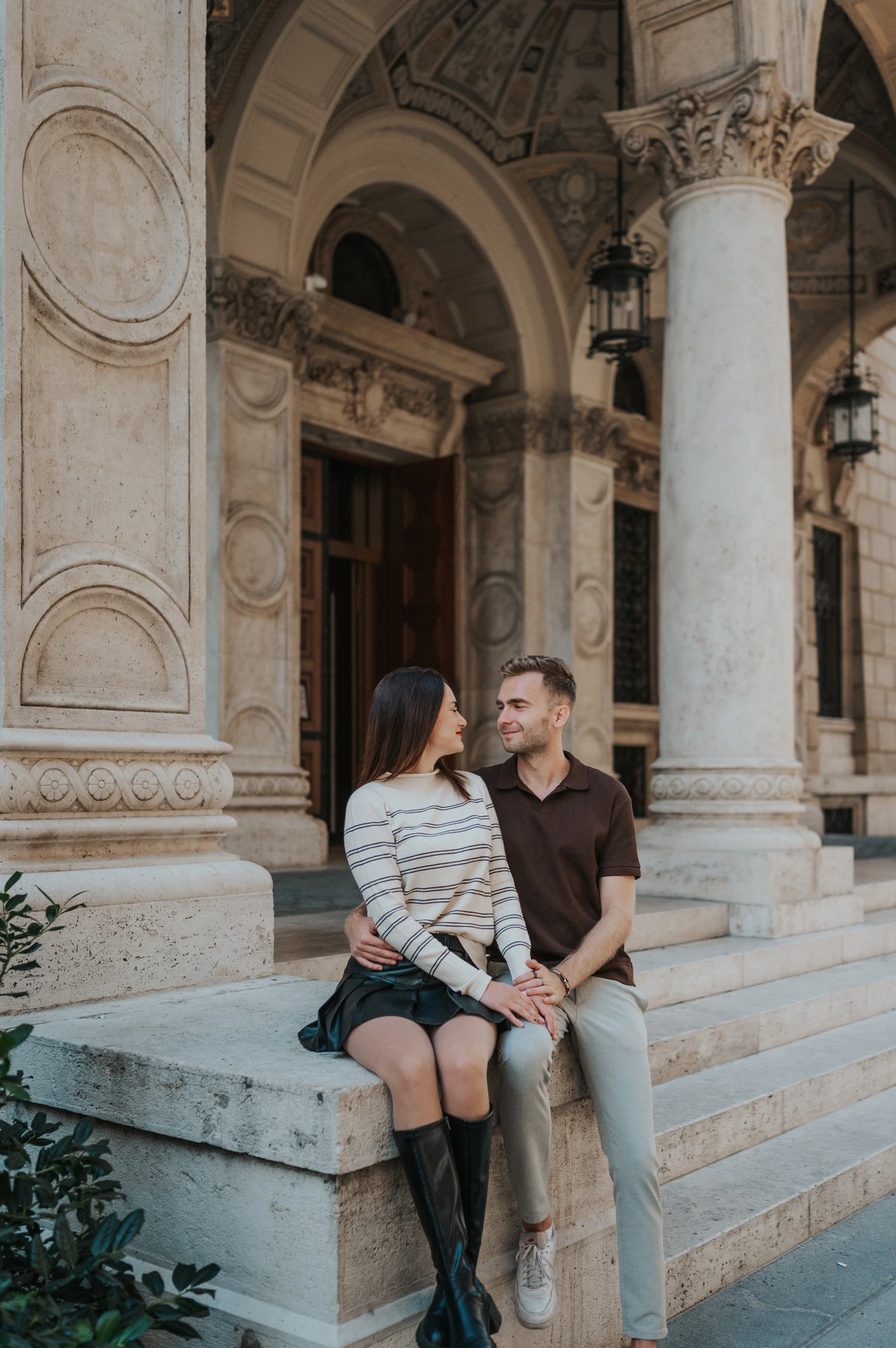 The couple sitting together on a stone plinth beneath the Opera’s ornate arches during a couple photoshoot in Budapest.