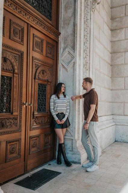 Budapest couple photoshoot: beside a carved Opera door The woman leaning beside a carved Opera door while her partner stands beside her during a couple photoshoot in Budapest.