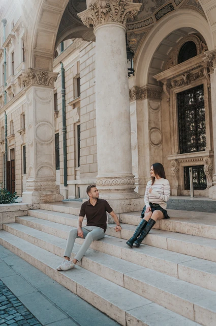 Budapest couple photoshoot: a wide view of the Opera steps The couple sitting apart on the broad Opera steps beneath carved stone arches during a couple photoshoot in Budapest.