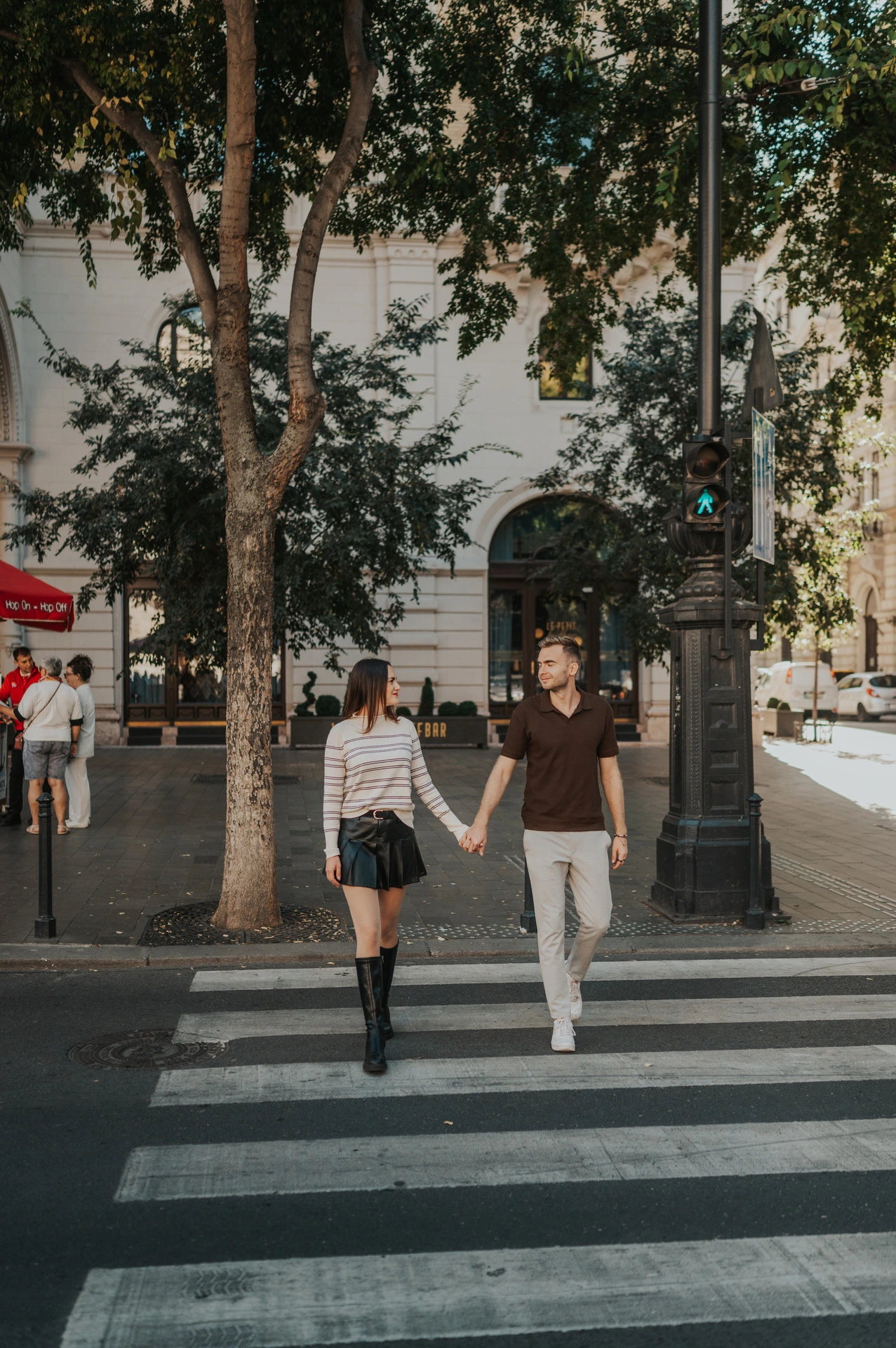 The couple walking hand in hand across a zebra crossing beside the Opera during a couple photoshoot in Budapest.