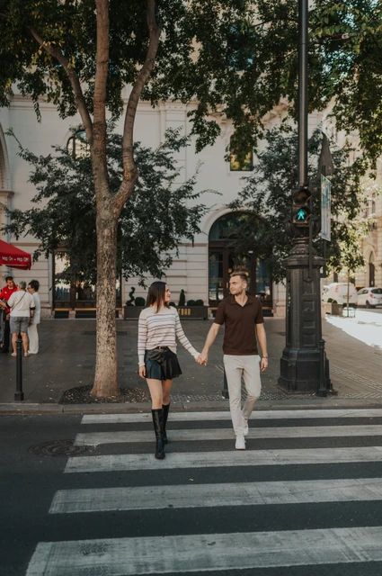 Budapest couple photoshoot: walking across a city-centre crossing The couple walking hand in hand across a zebra crossing beside the Opera during a couple photoshoot in Budapest.