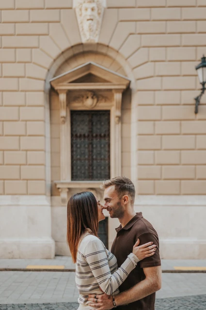 Budapest couple photoshoot: an embrace on a cobbled side street The couple embracing on a cobbled street beside a pale stone façade near the Opera during a couple photoshoot in Budapest.