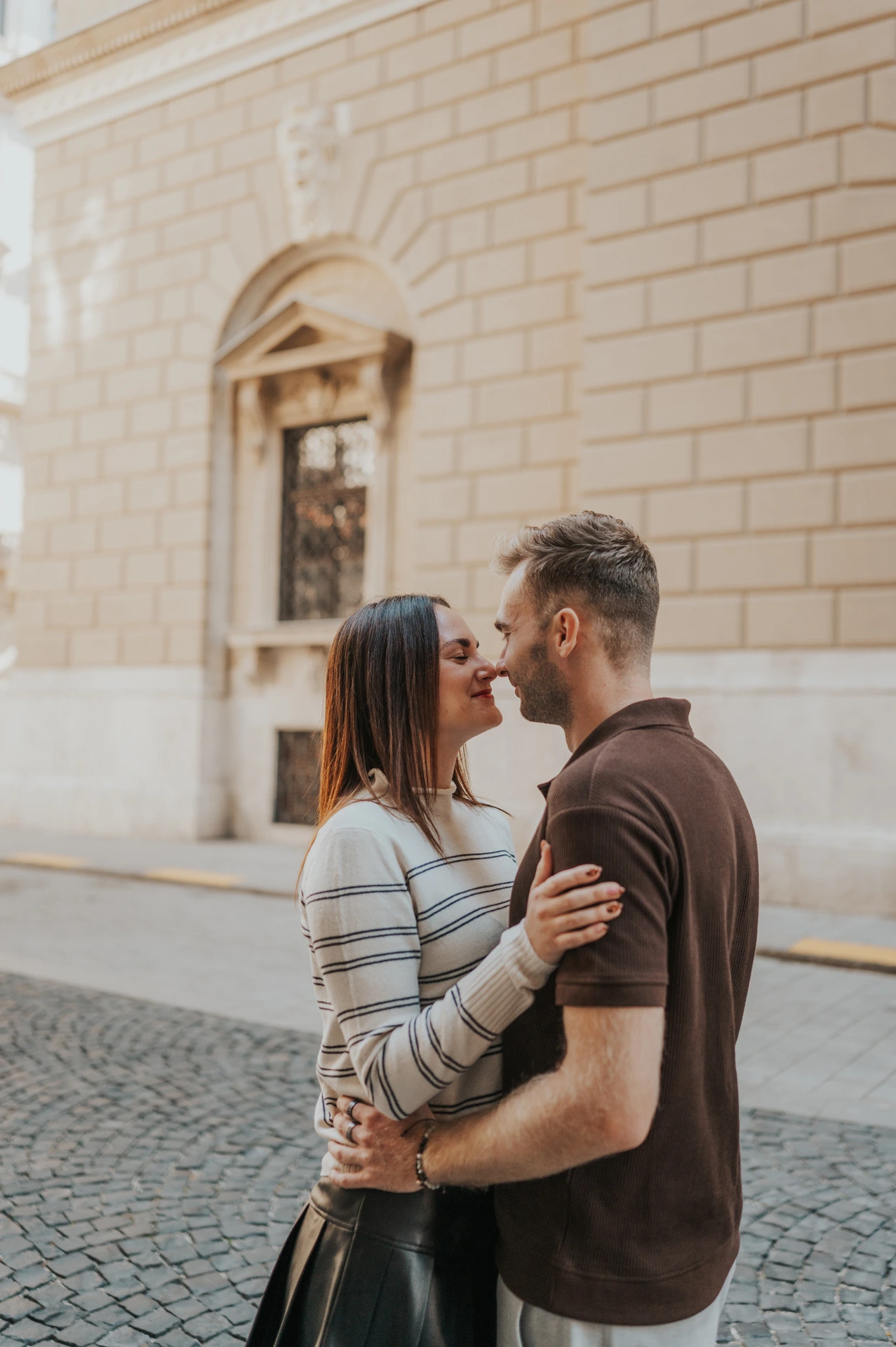 A closer portrait of the couple leaning towards each other on a cobbled street near the Opera during a couple photoshoot in Budapest.