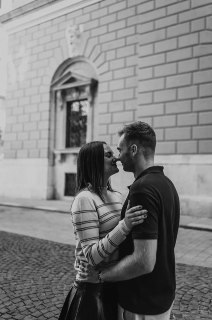 Budapest couple photoshoot: a close moment beside a pale stone wall in black and white Black-and-white photograph of the couple leaning close beside a pale stone wall on a cobbled street near the Opera during a couple photoshoot in Budapest.