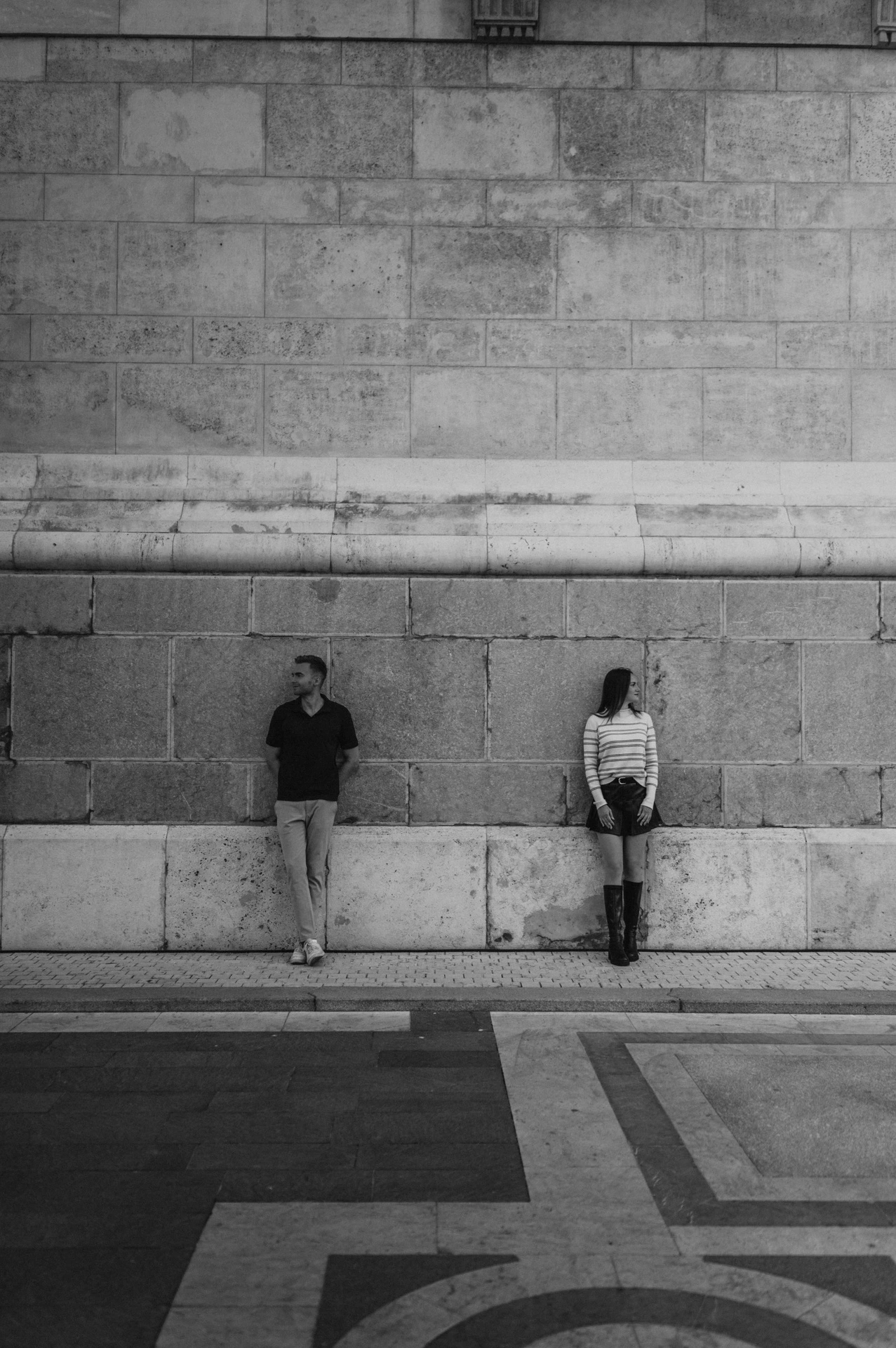 Black-and-white photograph of the couple standing on either side of a tall stone wall detail at St Stephen’s Basilica during a couple photoshoot in Budapest.