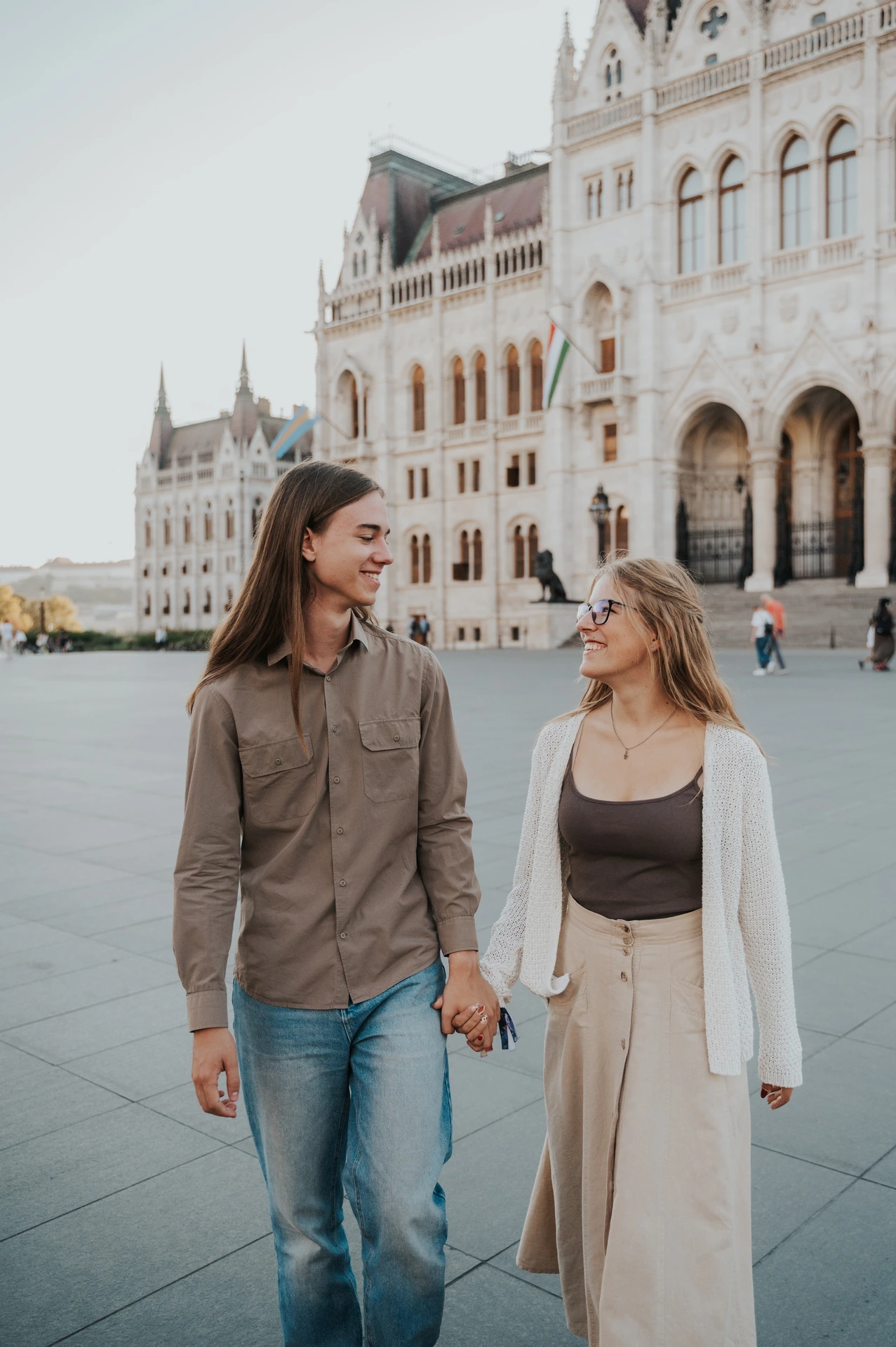 The couple holding hands and looking towards each other during their Budapest photoshoot, with Parliament’s arches behind them.