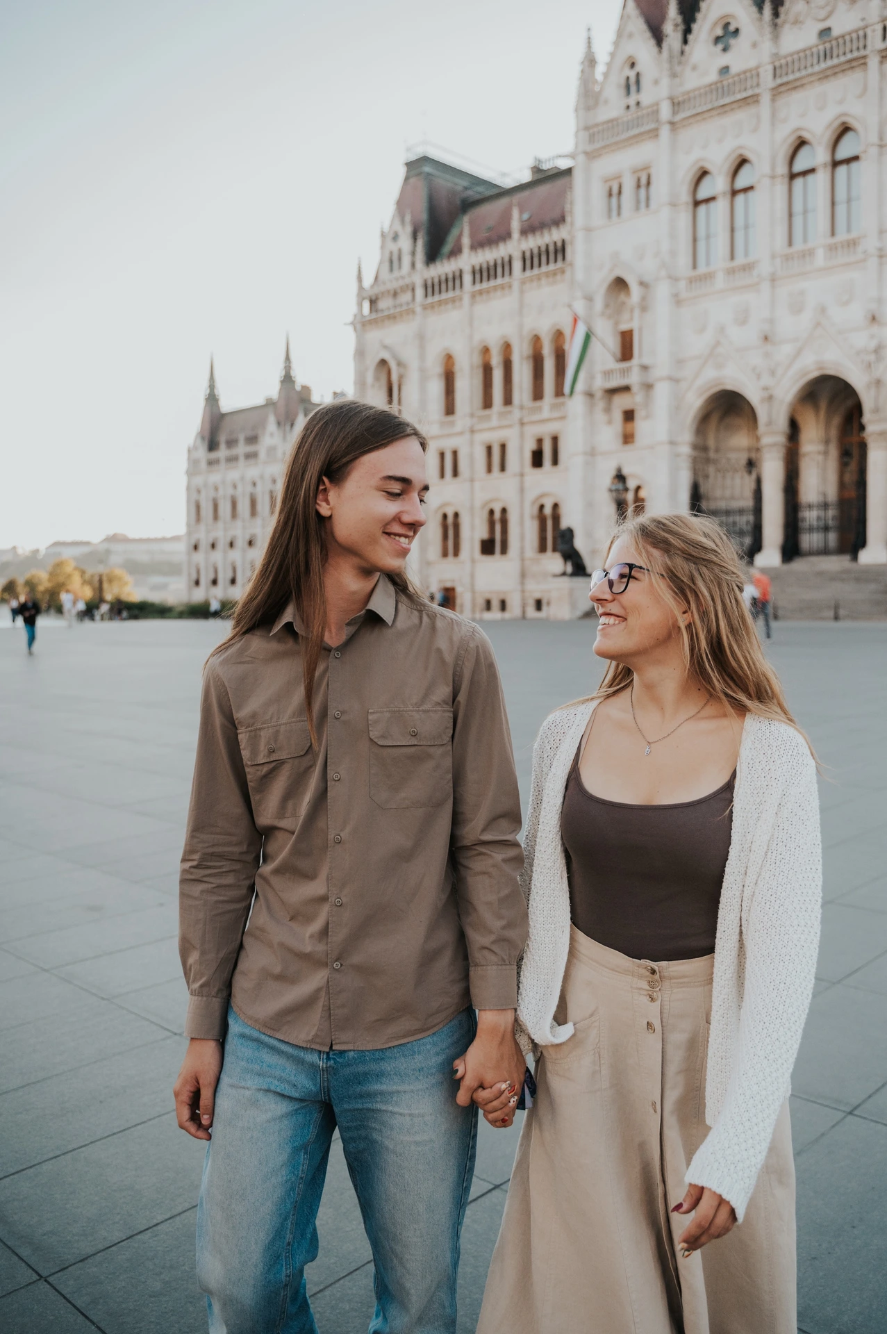 A close portrait of the couple smiling together during their Budapest photoshoot outside Parliament, one wearing a brown shirt and the other a white cardigan.