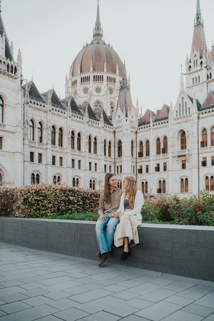 Photoshoot in Budapest seated beneath Parliament’s dome The couple seated together on a low stone ledge during their Budapest photoshoot, with Parliament’s dome rising above them.