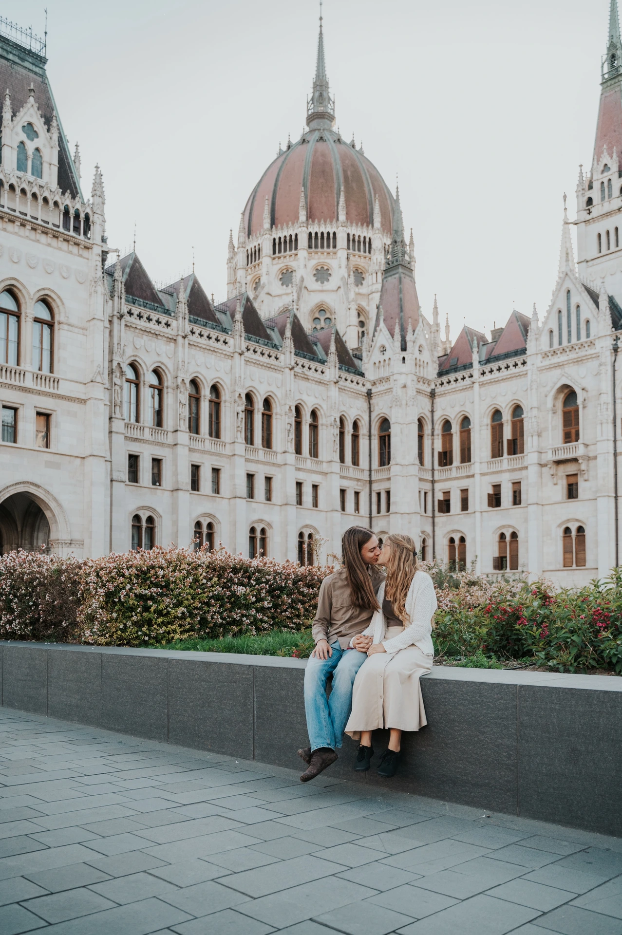 A wide portrait of the seated couple during their Budapest photoshoot, with Parliament’s dome and detailed stonework filling the background.