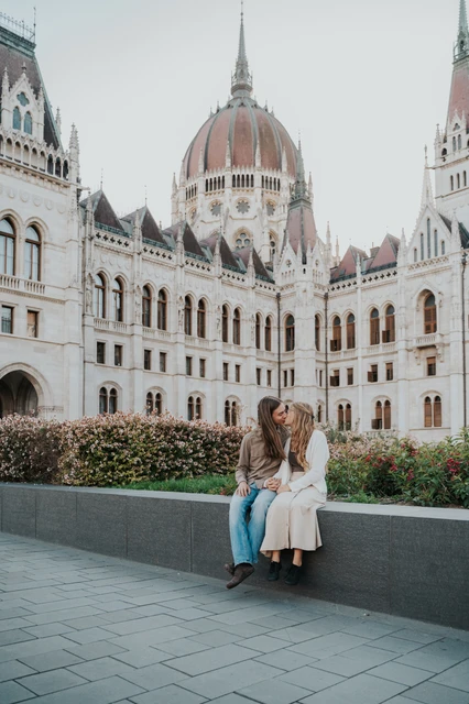 Budapest photoshoot with Parliament framing the seated couple A wide portrait of the seated couple during their Budapest photoshoot, with Parliament’s dome and detailed stonework filling the background.