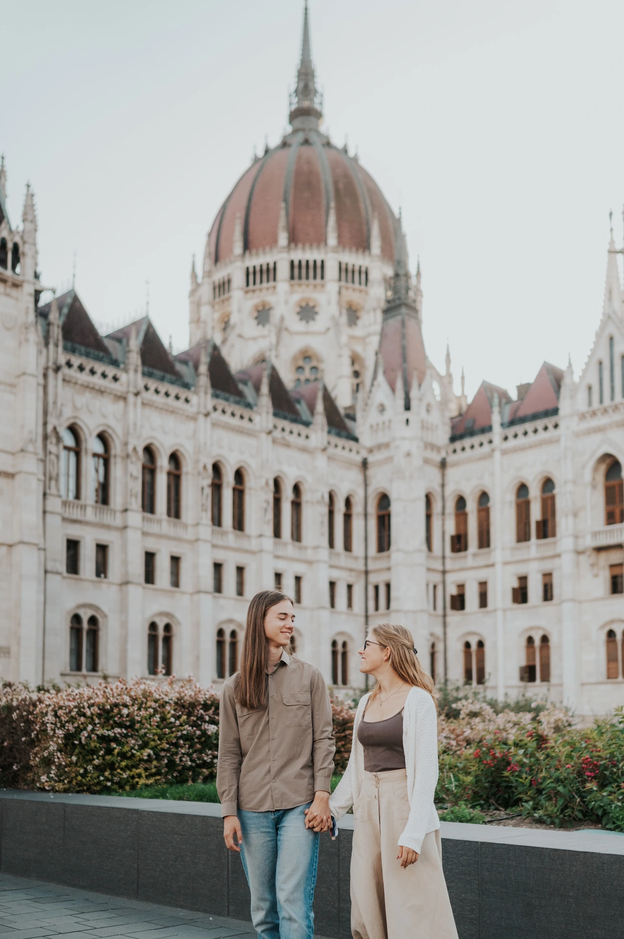 The couple looking towards each other beside the garden during their Budapest photoshoot, with the Hungarian Parliament filling the background.