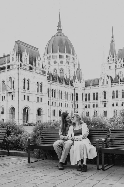 Budapest photoshoot on the Parliament bench in black and white Black-and-white photograph of the couple seated together on a bench during their Budapest photoshoot beside the Hungarian Parliament.