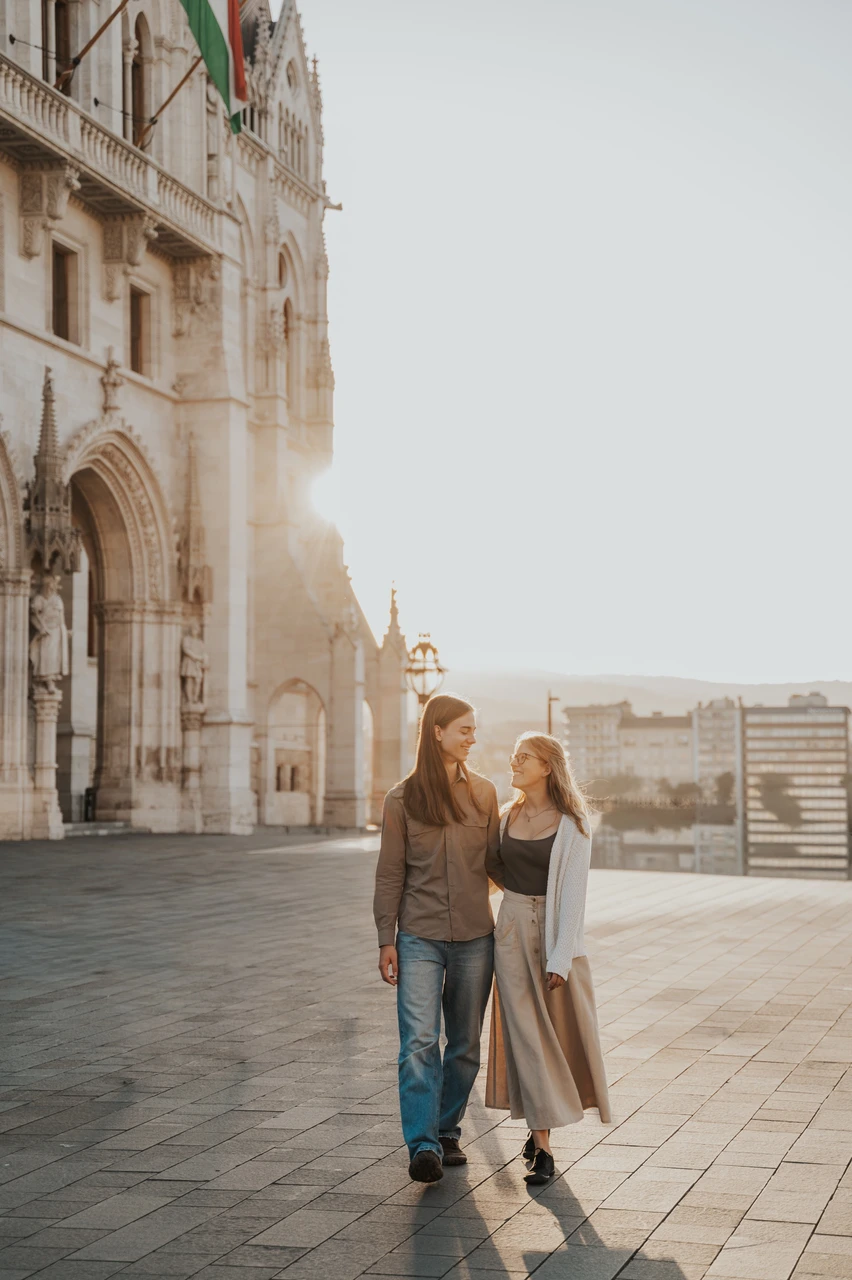 Couple photoshoot in Budapest beside Parliament’s sunlit façade The couple holding each other close beside Parliament during their Budapest photoshoot, with warm evening light falling along the façade.