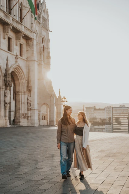 The couple holding each other close beside Parliament during their Budapest photoshoot, with warm evening light falling along the façade.