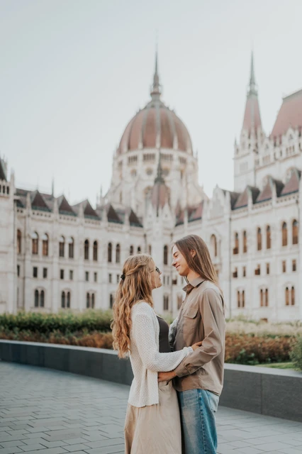 Budapest photoshoot embracing with Parliament’s dome in the backdrop The couple facing each other in an embrace during their Budapest photoshoot, with Parliament’s dome and flowerbeds behind them.