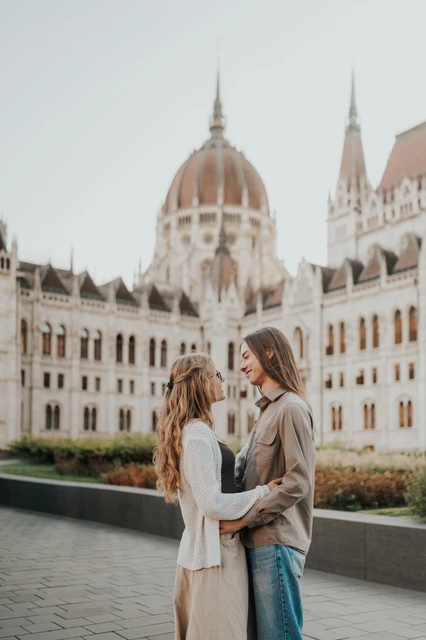 Budapest couple photoshoot sharing a close moment beneath Parliament’s dome The couple leaning towards each other in front of Parliament during their Budapest photoshoot, with the dome rising above the garden.