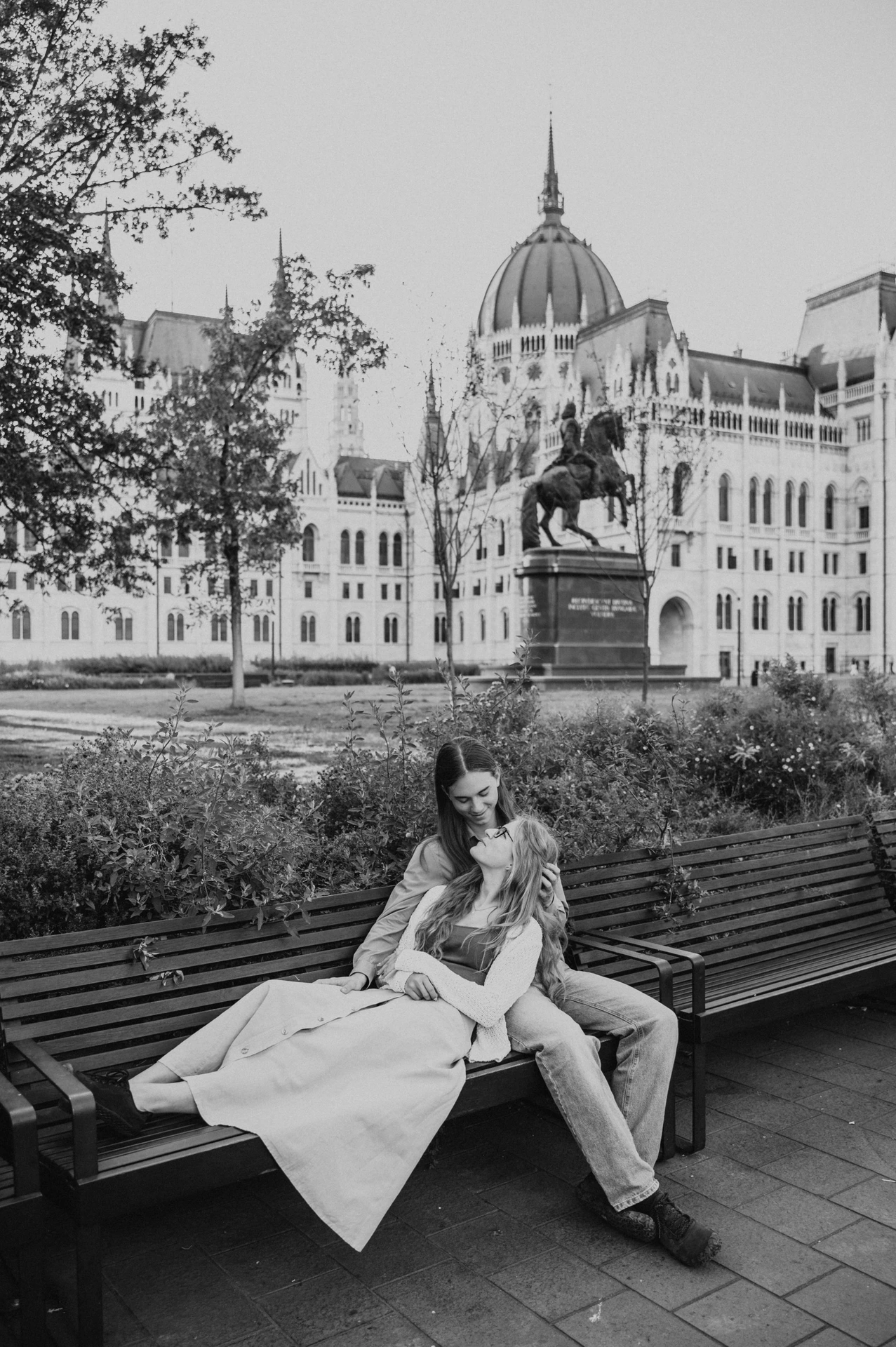 Black-and-white photograph of the couple relaxing together on the wooden bench during their Budapest photoshoot near Parliament.
