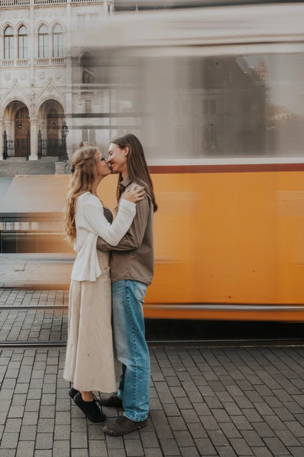 Budapest couple photoshoot with a passing tram beside Parliament The couple holding each other close during their Budapest photoshoot, with a moving yellow tram and Parliament’s stone façade behind them.
