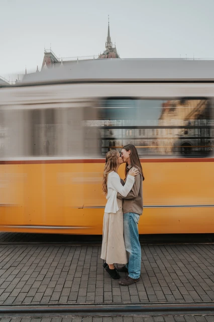 Budapest photoshoot with a yellow tram beneath Parliament’s dome The couple embracing during their Budapest photoshoot, with a yellow tram passing behind them and Parliament’s dome visible above it.
