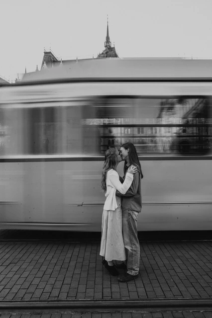 Budapest couple photoshoot with a tram and Parliament’s dome in black and white Black-and-white view of the couple embracing during their Budapest photoshoot, with a passing tram and Parliament’s dome behind them.