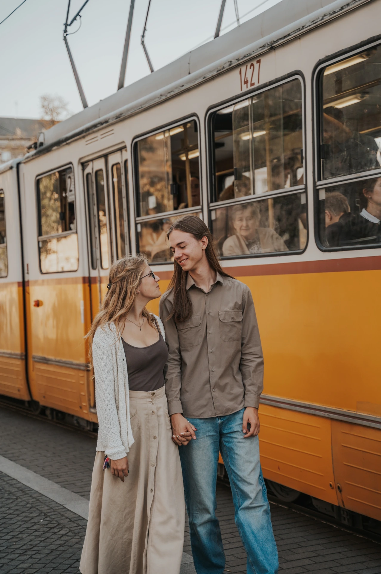 A closer portrait of the couple smiling at each other during their Budapest photoshoot beside the windows of a yellow tram.