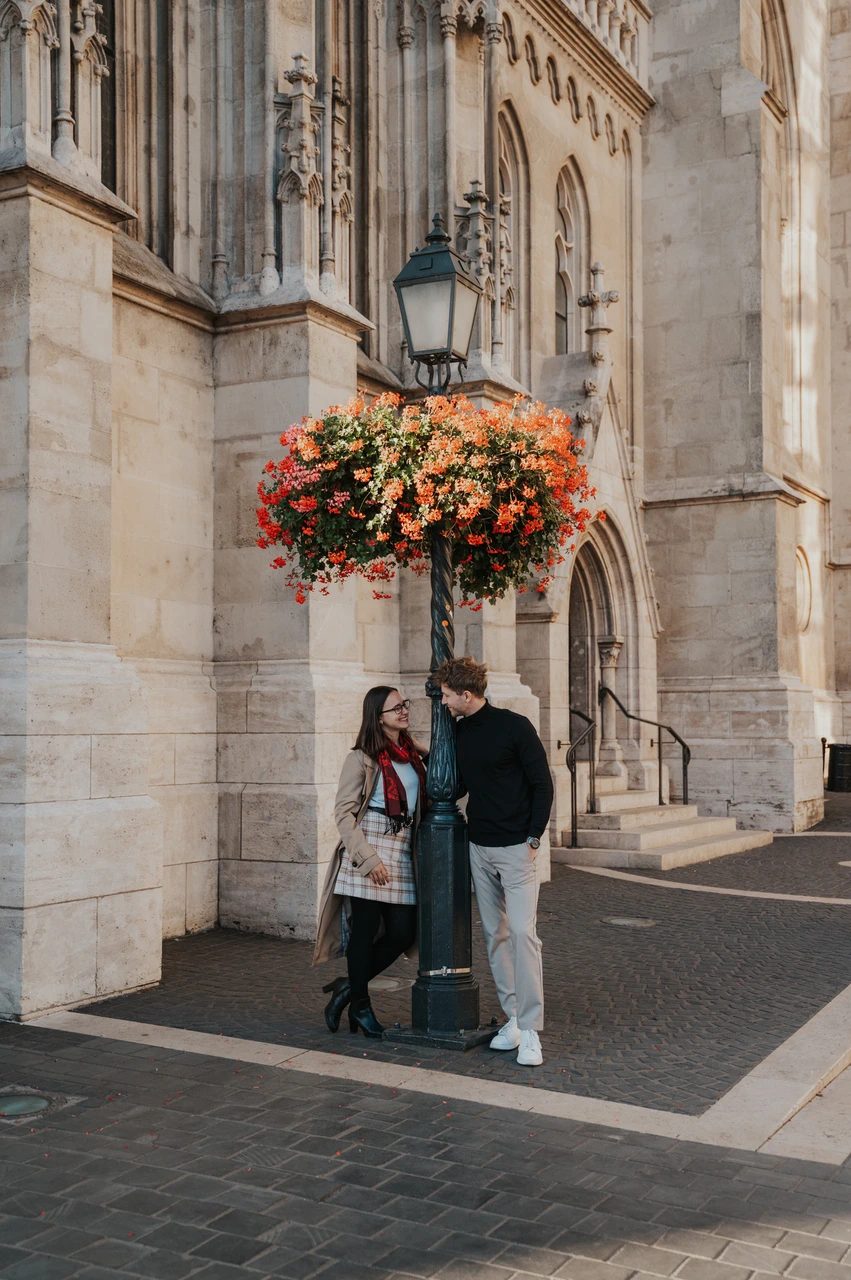 Budapest couple photoshoot: orange flowers beside Matthias Church The couple standing beside a basket of orange flowers against Matthias Church’s pale stone façade during a couple photoshoot in Budapest.