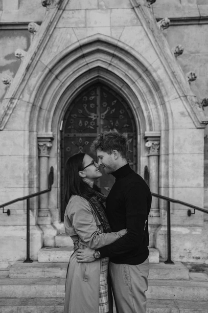 Budapest couple photoshoot: a kiss by the carved wooden door in black and white Black-and-white photograph of the couple kissing in front of Matthias Church’s carved wooden doorway during a couple photoshoot in Budapest.