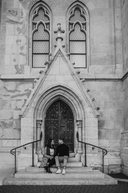 Budapest couple photoshoot: the church’s carved stone façade in black and white Wide black-and-white portrait of the couple beneath Matthias Church’s pointed doorway and carved stone windows during a couple photoshoot in Budapest.