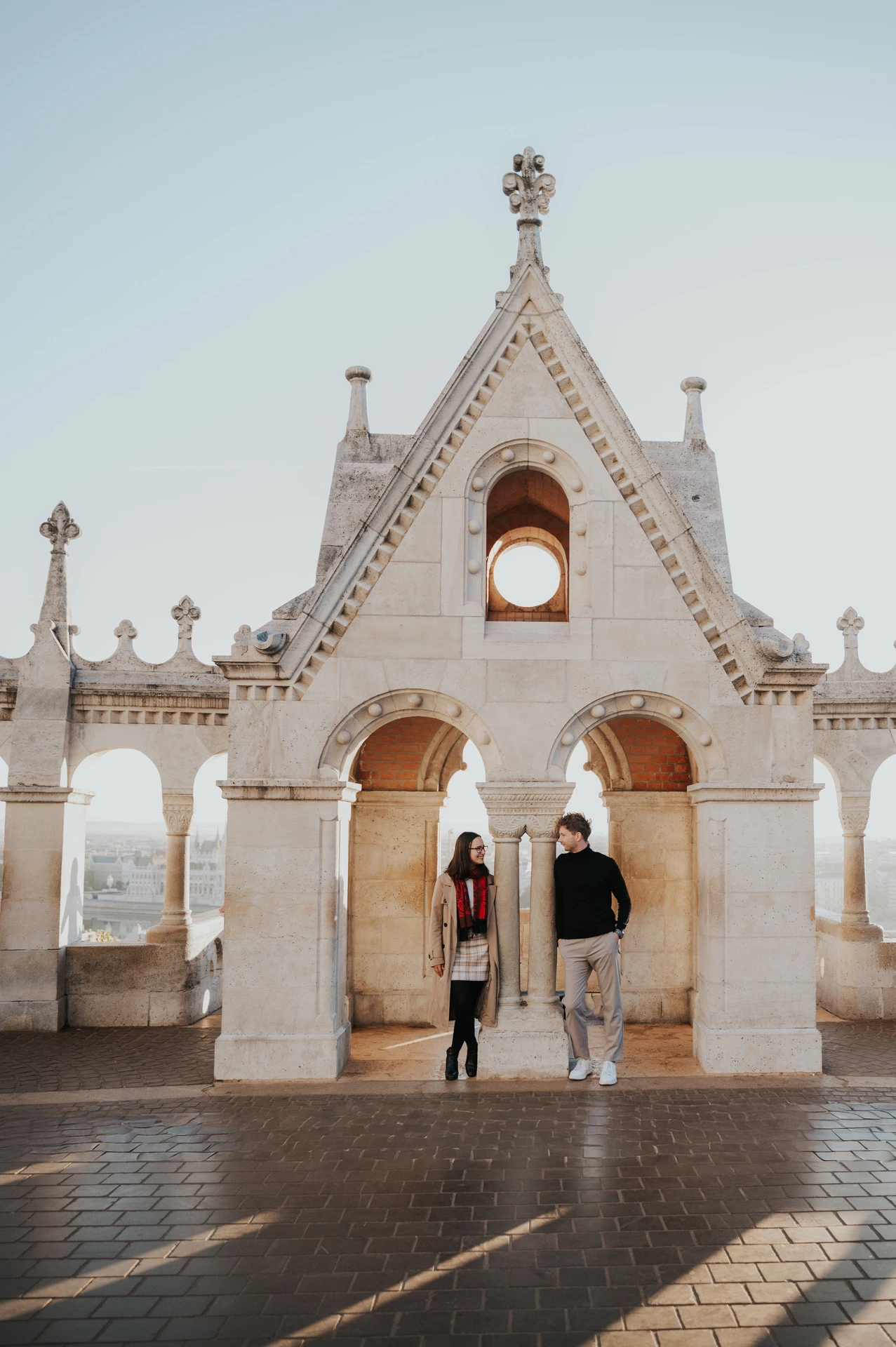 The couple standing beneath the ornate gabled arch at Fisherman’s Bastion during a couple photoshoot in Budapest.
