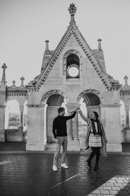Budapest couple photoshoot: a dance beneath the stone arch in black and white Black-and-white photograph of the couple dancing beneath the ornate gabled arch at Fisherman’s Bastion during a couple photoshoot in Budapest.