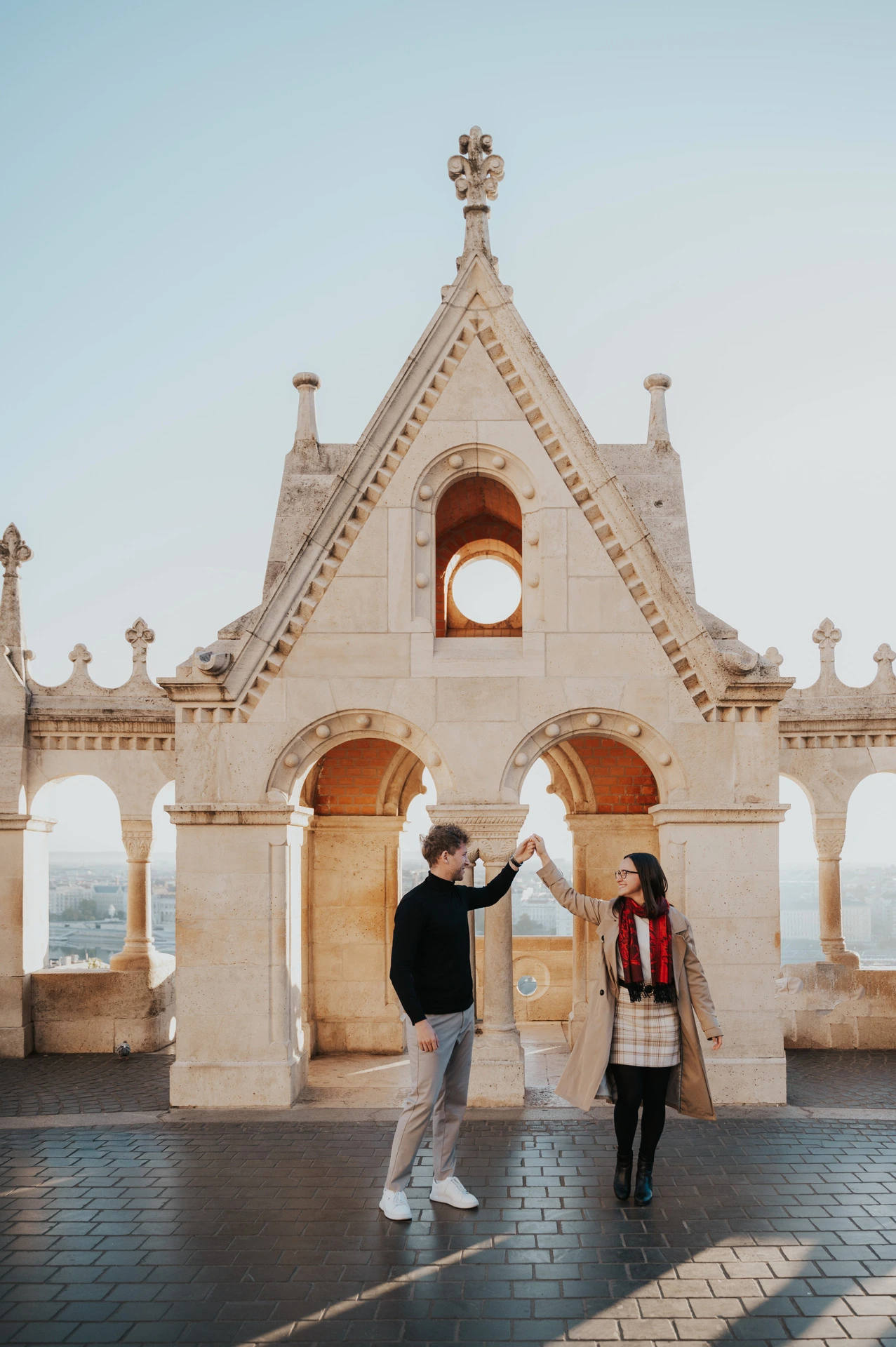 The couple turning towards each other beneath Fisherman’s Bastion’s gabled arch during a couple photoshoot in Budapest.