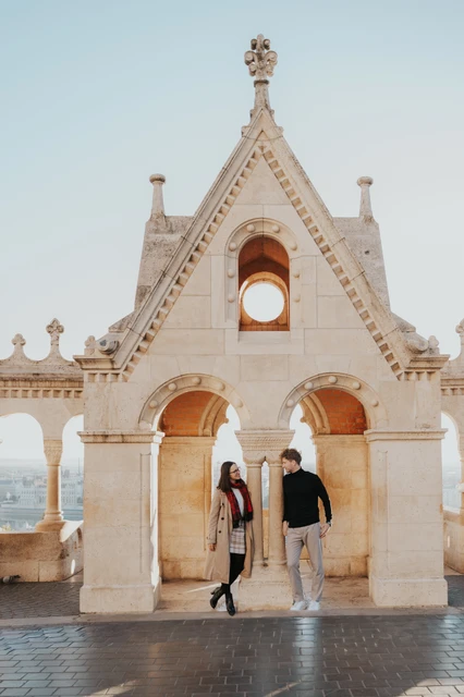 Budapest couple photoshoot: walking beneath the ornate gable The couple walking together beneath Fisherman’s Bastion’s ornate gabled arch during a couple photoshoot in Budapest.