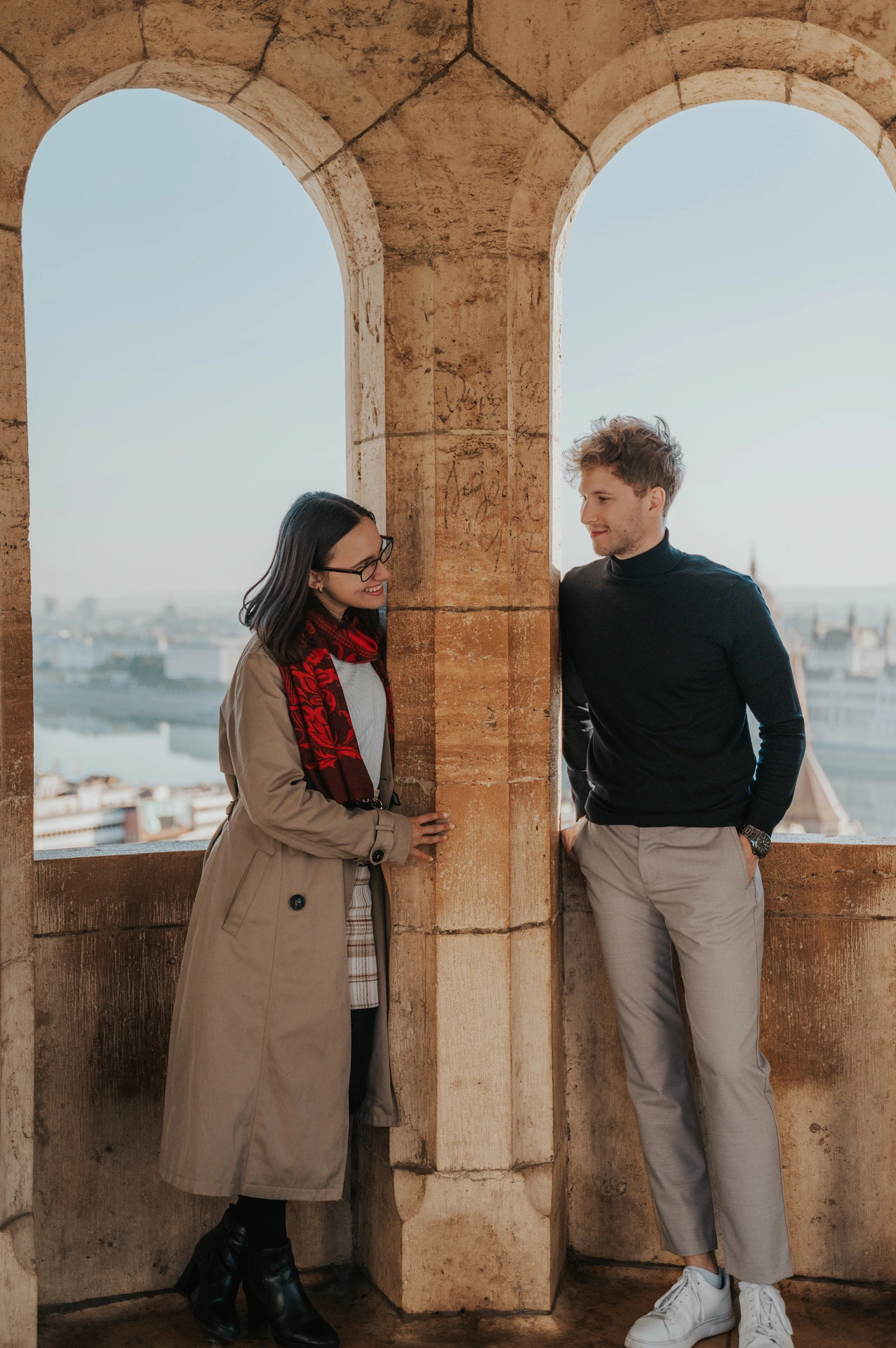 The couple looking towards each other from either side of a stone column inside Fisherman’s Bastion’s arcade during a couple photoshoot in Budapest.