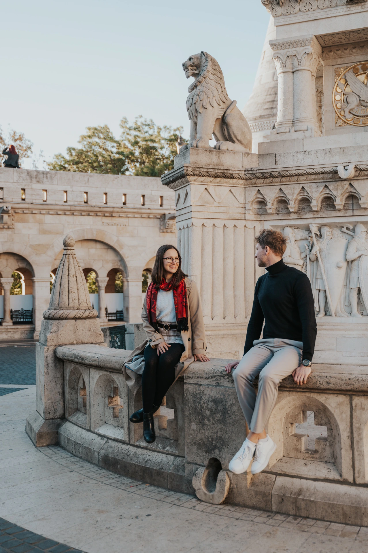The couple sitting on a carved stone monument with the Bastion’s arcade behind them during a couple photoshoot in Budapest.