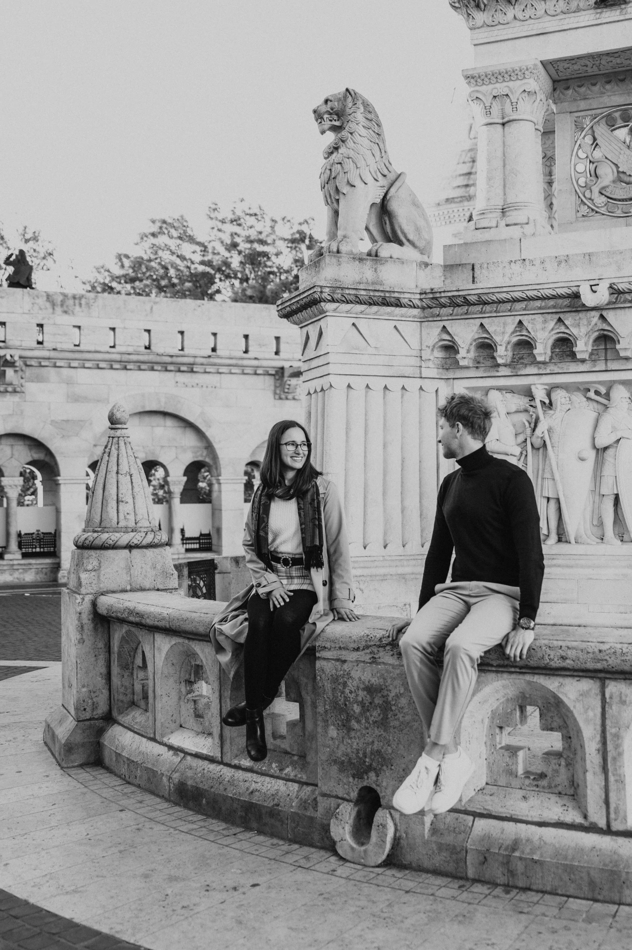 Black-and-white photograph of the couple sitting together by a stone monument near Fisherman’s Bastion during a couple photoshoot in Budapest.