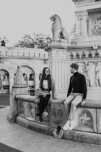 Budapest couple photoshoot: a seated portrait beside the monument in black and white Black-and-white photograph of the couple sitting together by a stone monument near Fisherman’s Bastion during a couple photoshoot in Budapest.
