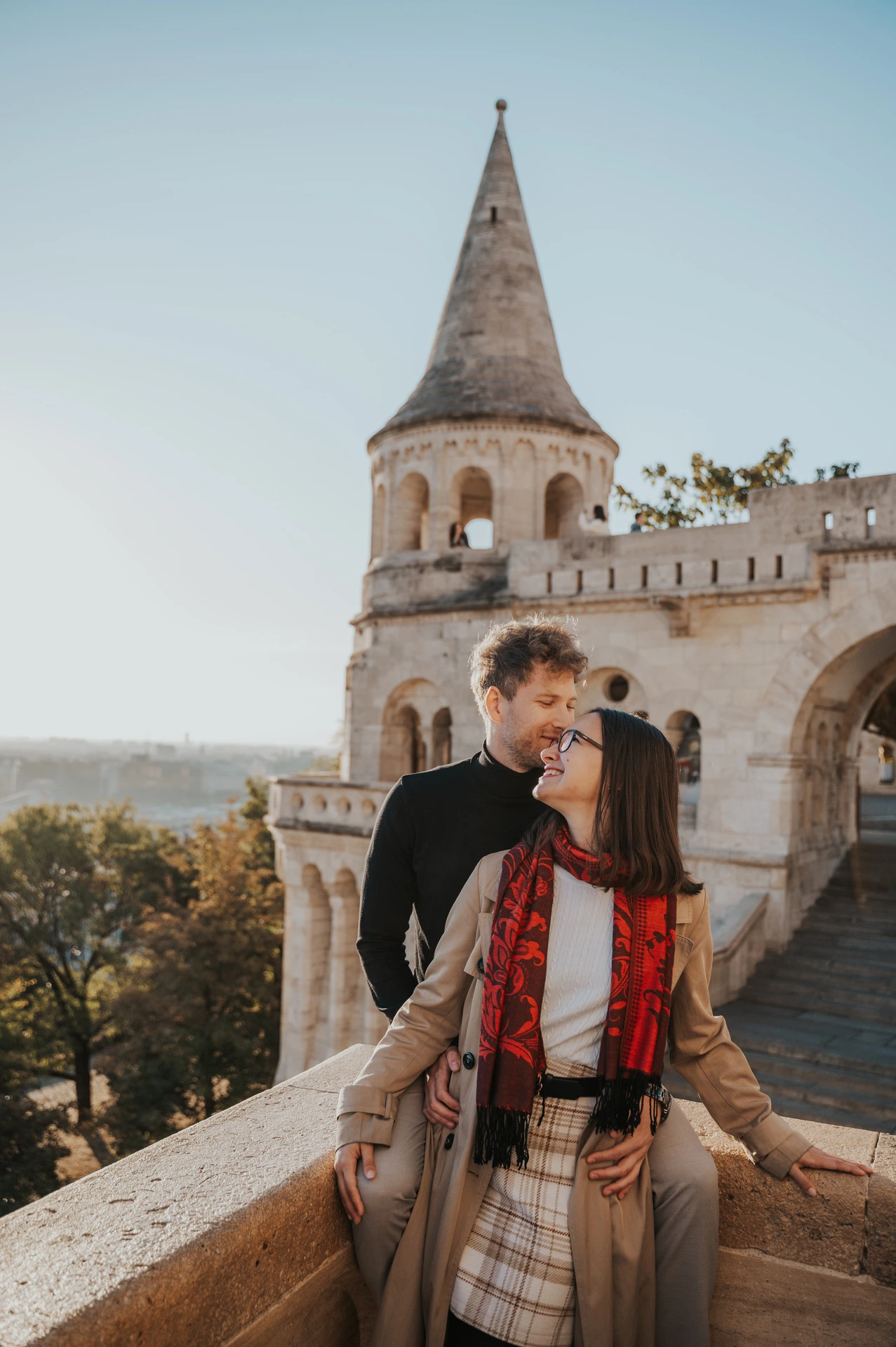 The man kissing his partner near her temple beside Fisherman’s Bastion’s stone balustrade during a couple photoshoot in Budapest.